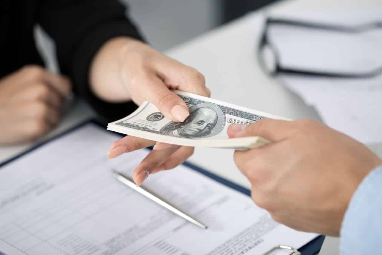 woman handing man a stack of cash over a desk