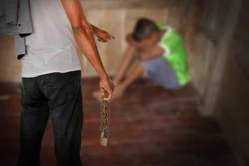 man holding a chain pointing at a child who is hiding in the corner scared