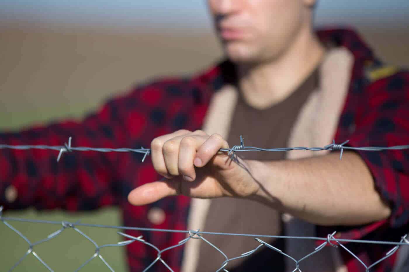 man resting his hands on a barbed wire fence