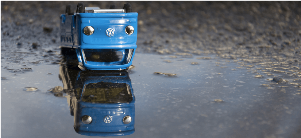 blue toy VW van upside down in a puddle with a reflection of the van the right way round