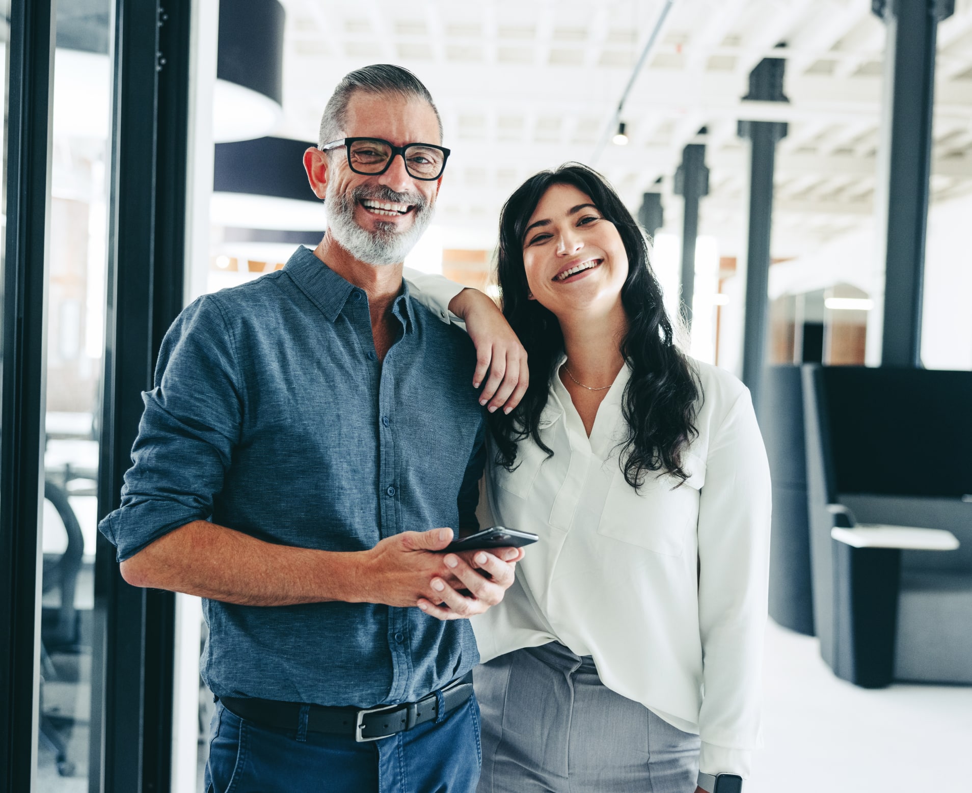 woman with her arm leaning on a man's shoulder in an office, both smiling at the camera