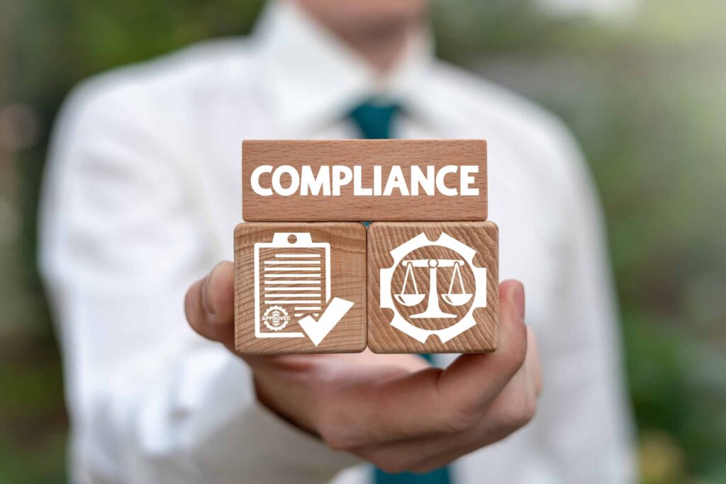 man holding three wooden blocks, two have logos, one has the text 'compliance' on it