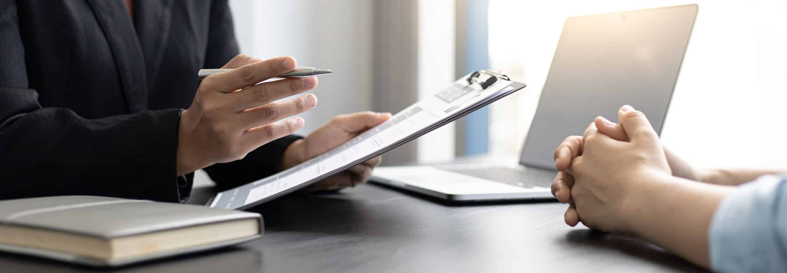 Image of two people at a desk, close up of their hands showing a third party investigative interview taking place