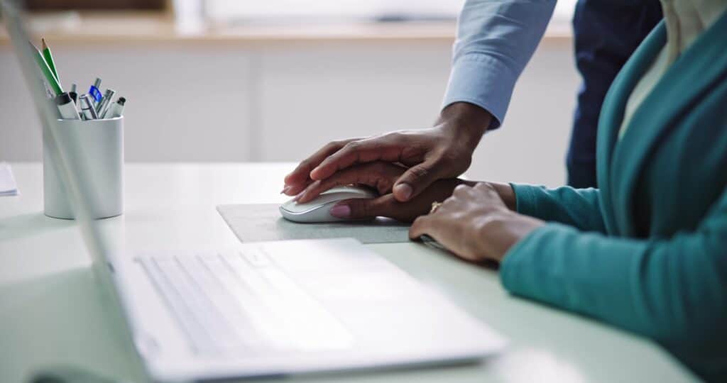 Man placing his hand on top of his female colleagues on her mouse inappropriately