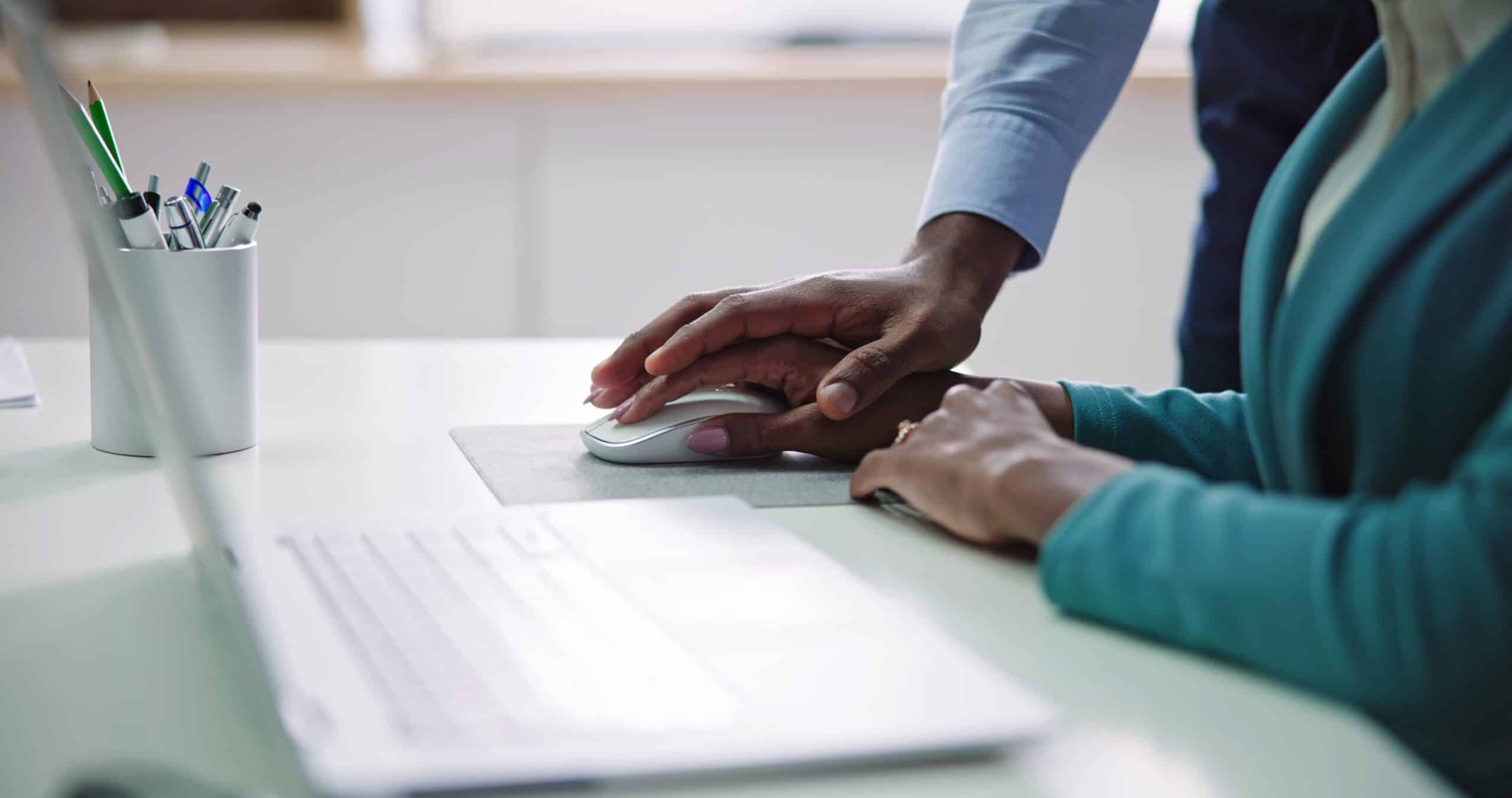 Man placing his hand on top of his female colleagues on her mouse inappropriately