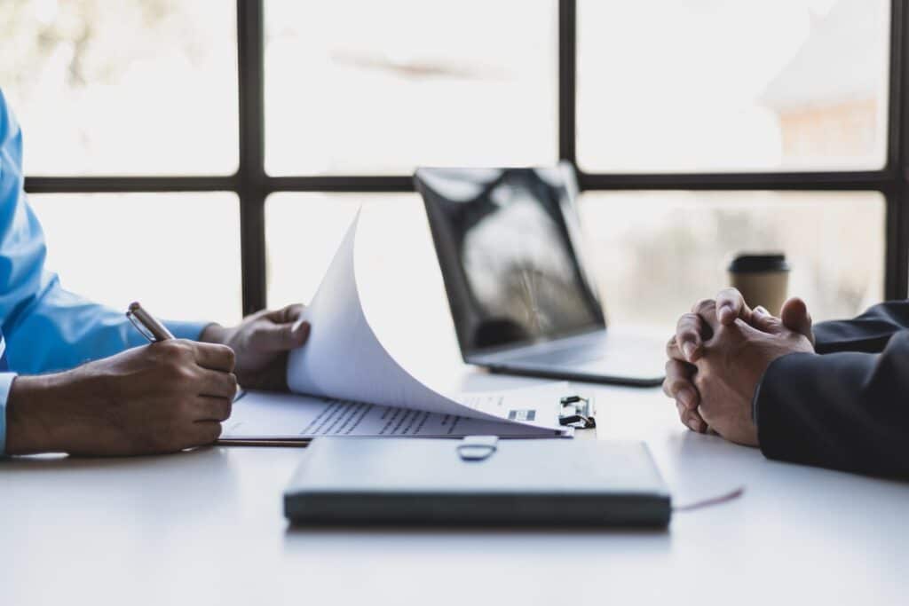 Two people at across from eachother at a desk, one signing a contract