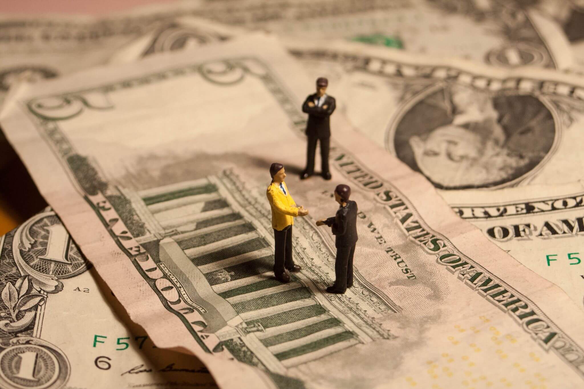 three miniature toy people standing on top of a pile of bank notes