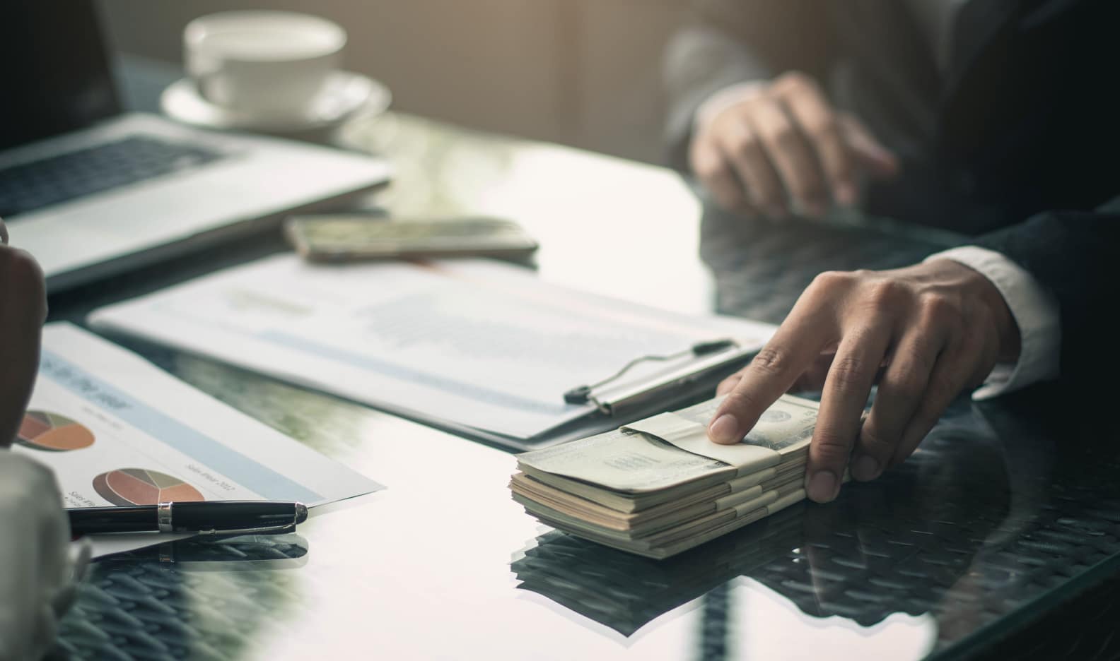 Man in a suit sliding a pile of cash across a table