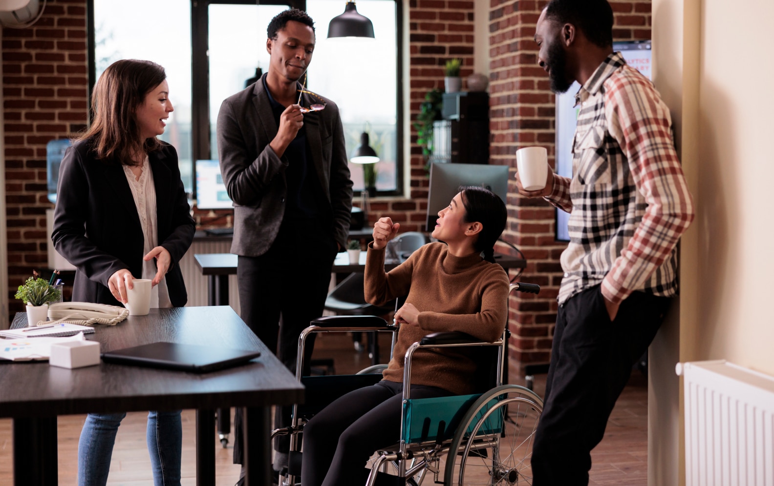 colleagues speaking around a desk, one in a wheelchair and the rest standing