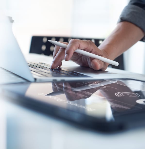 close up of a hand working on a laptop with a tablet device next to it