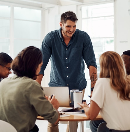 Man standing with his hands on a table that is being sat around by a team of people