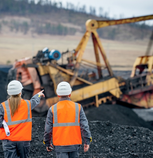 Two people on a mining site wearing hard hats and high visibility vests pointing to the distance