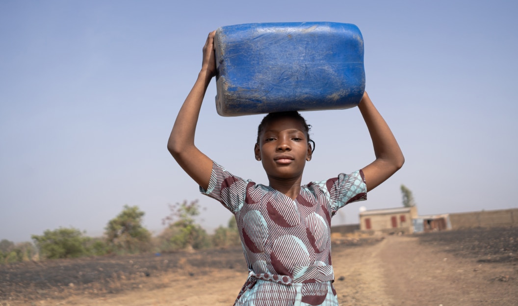 girl carrying a water carrier on her head in a desolate area