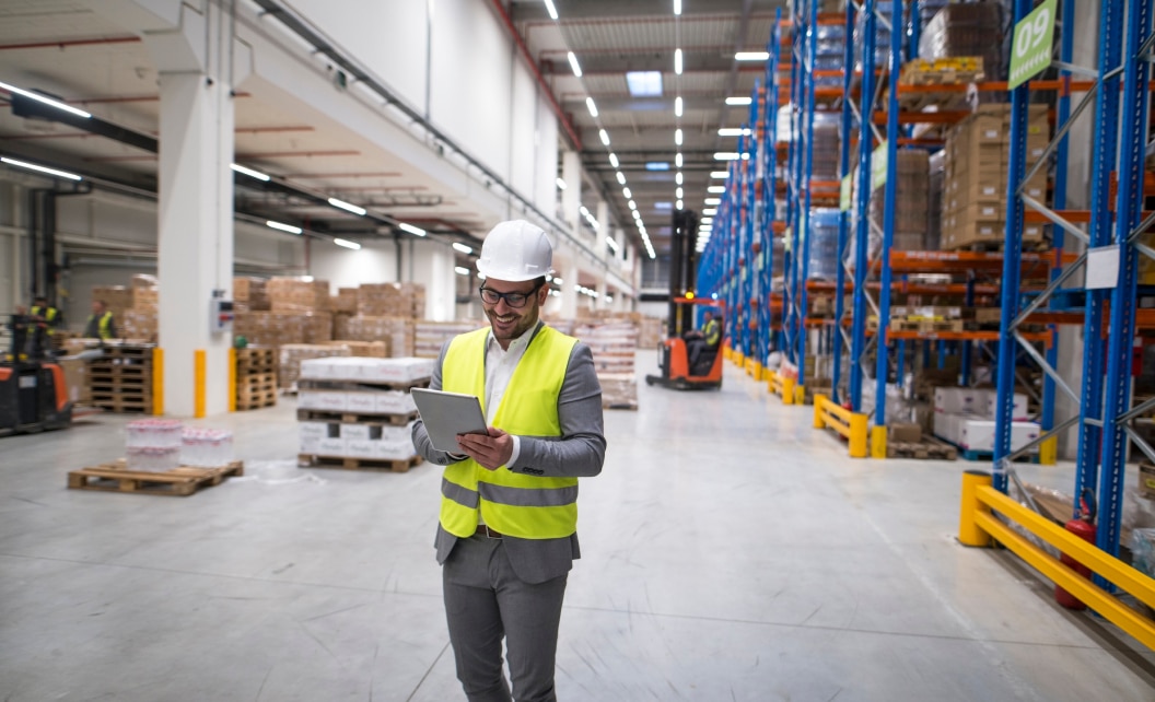 warehouse manager walking through a large storage area holding a tablet