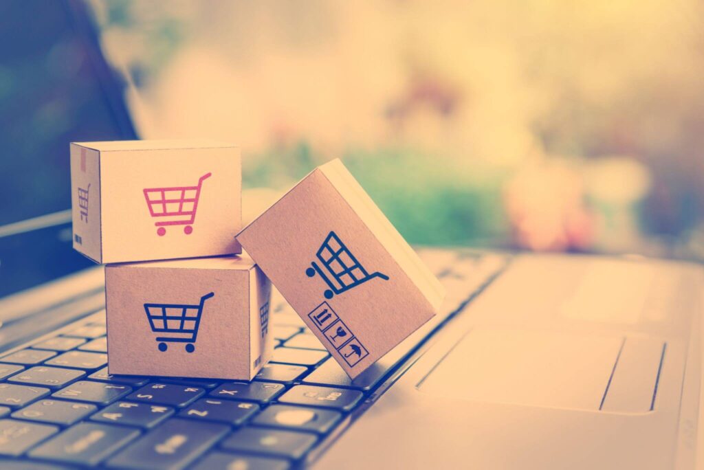 three small cardboard boxes balancing on a laptop keyboard with shopping carts printed on them