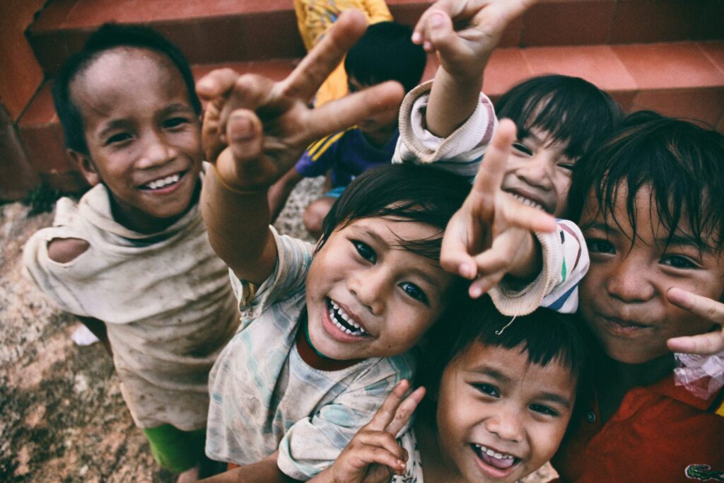 Children smiling looking up at the camera making peace signs with their hands