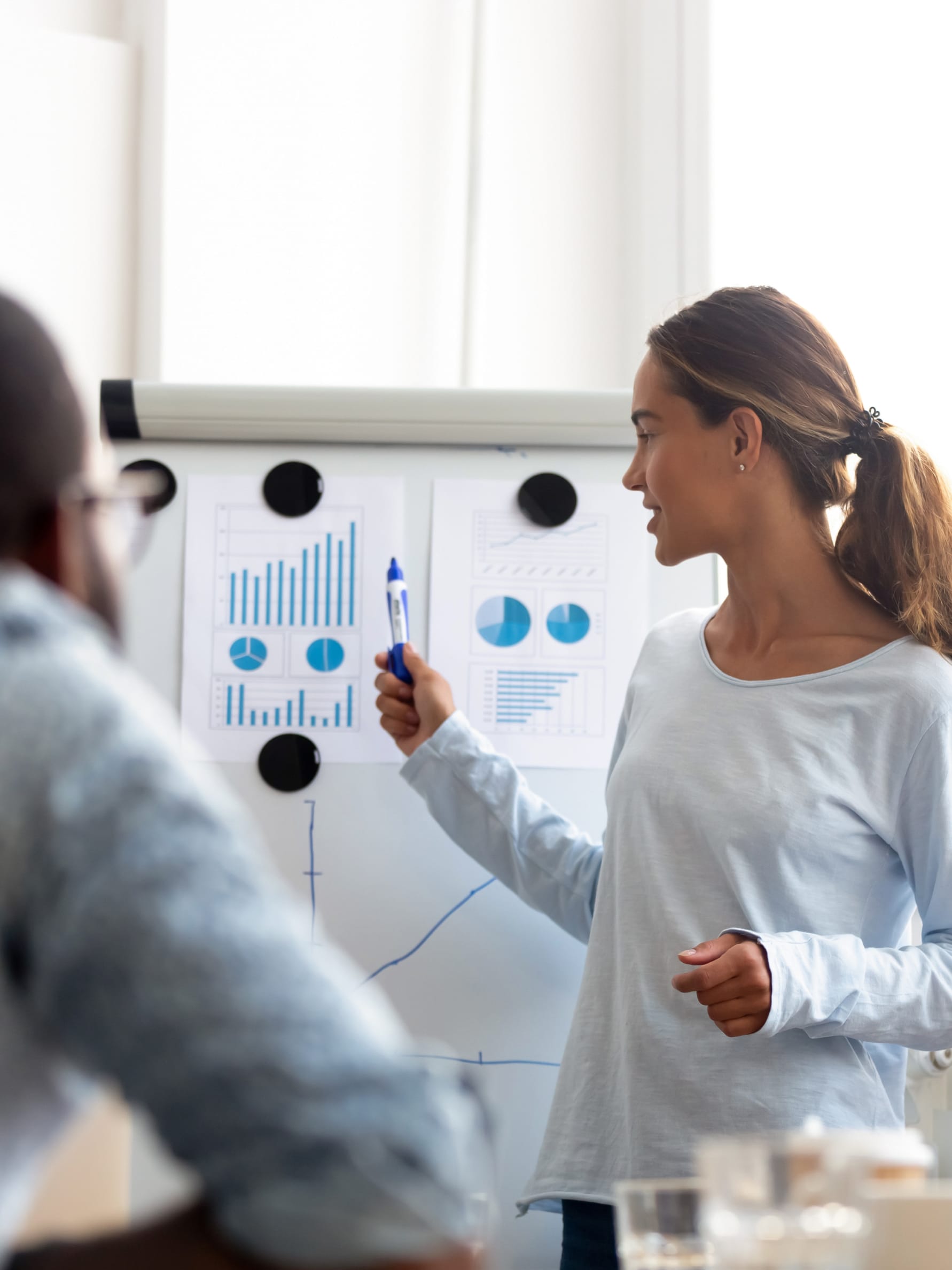 woman giving a presentation pointing to various graphs on a whiteboard