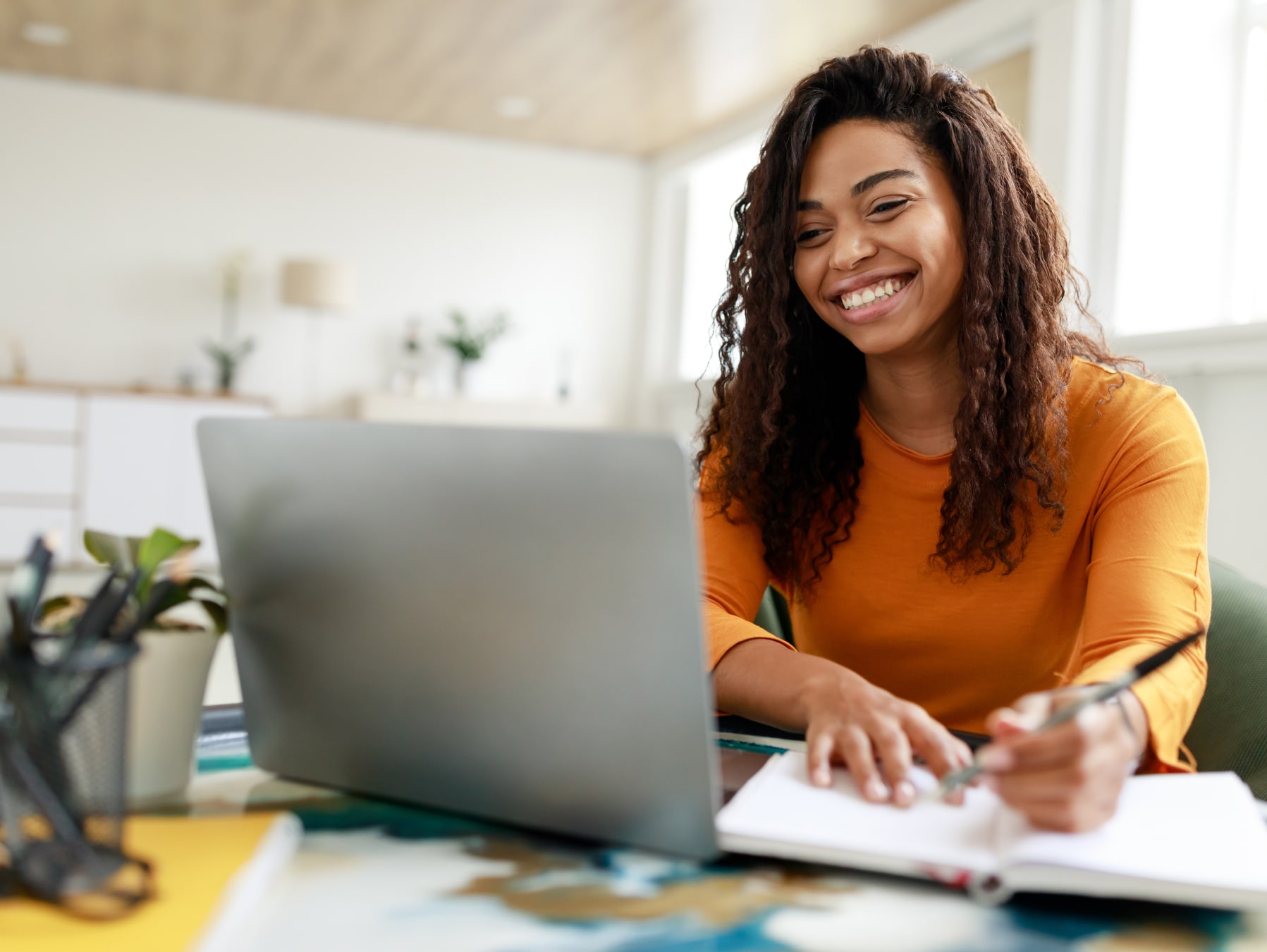 Woman making notes and smiling while on a video call on her laptop