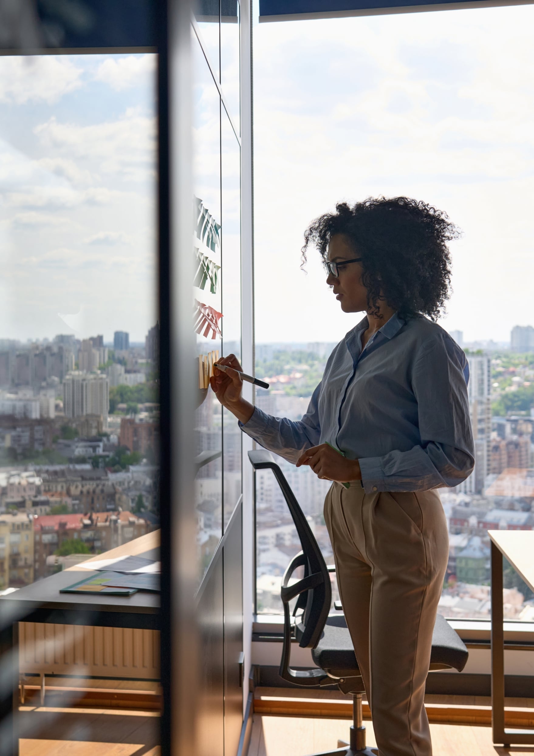 Woman writing on a sticky note that is on an office wall