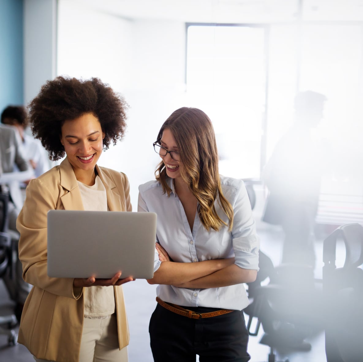 two women standing in an office looking at a laptop screen and smiling