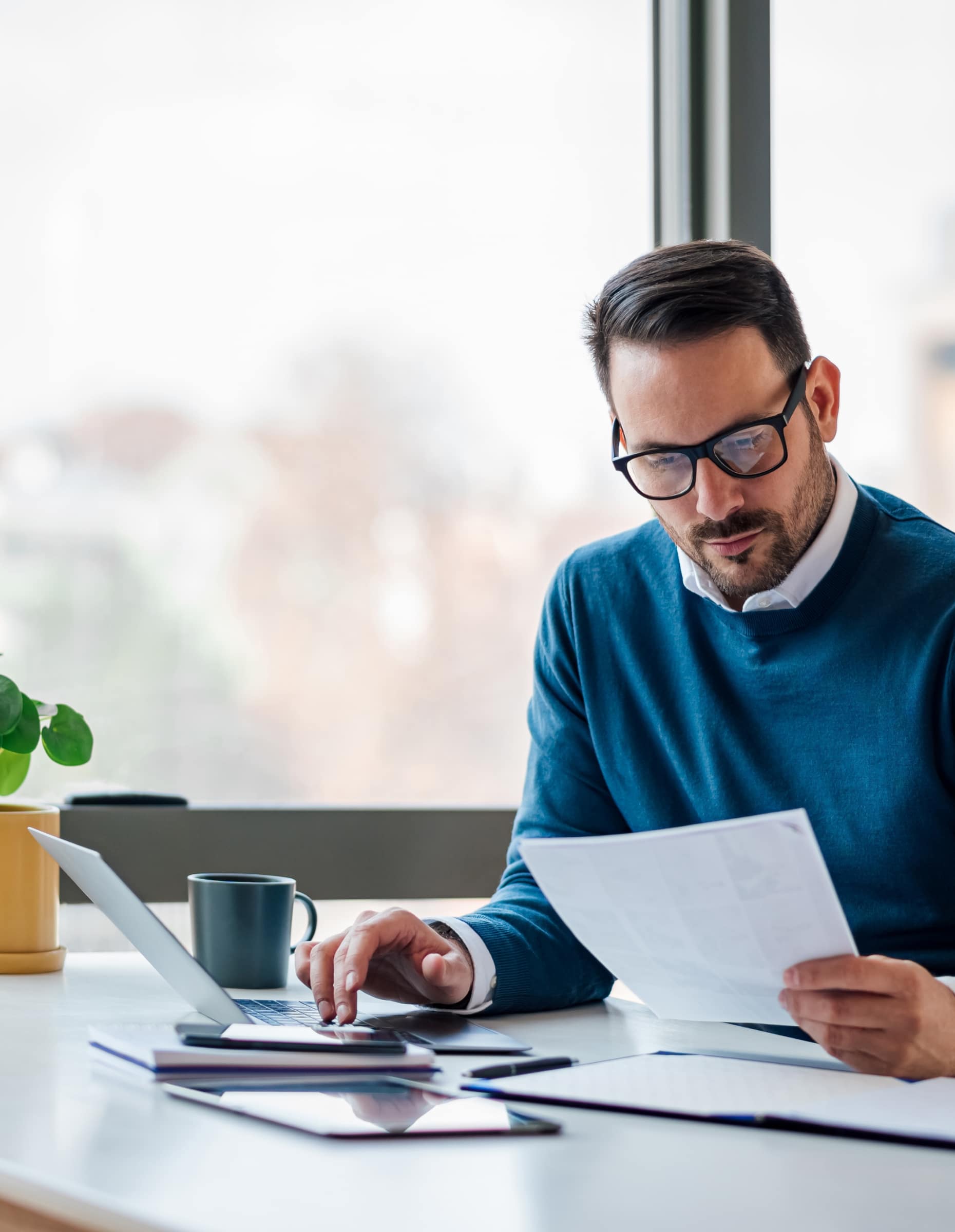 Man reading a document while sat at his desk in front of his laptop