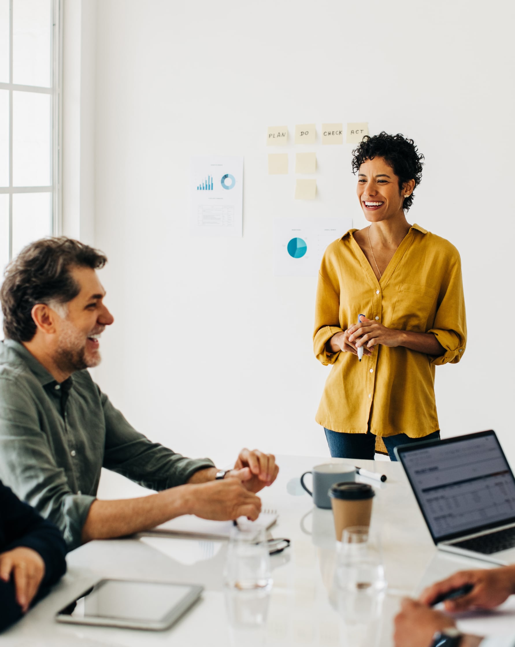 Woman leading a team meeting, standing at the head of the table smiling