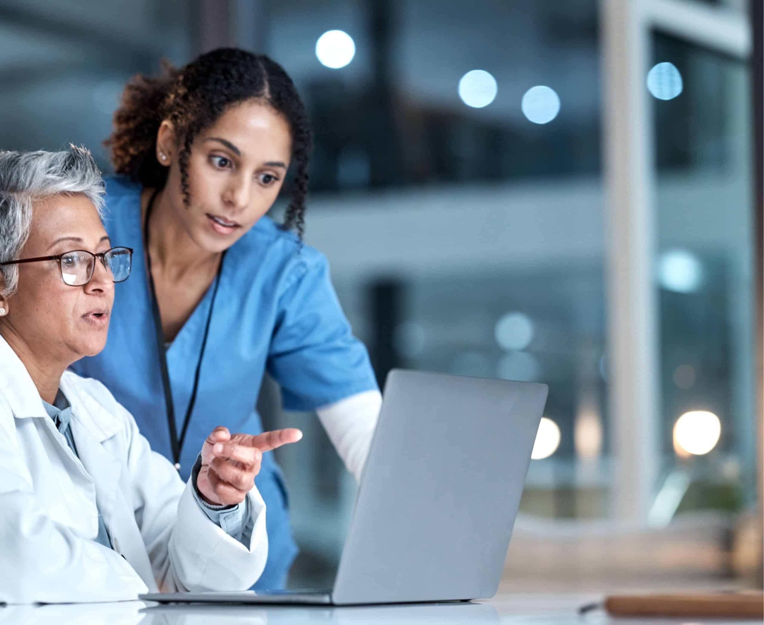 Woman sat at a desk asking a question to her colleague next to her pointing at a laptop screen