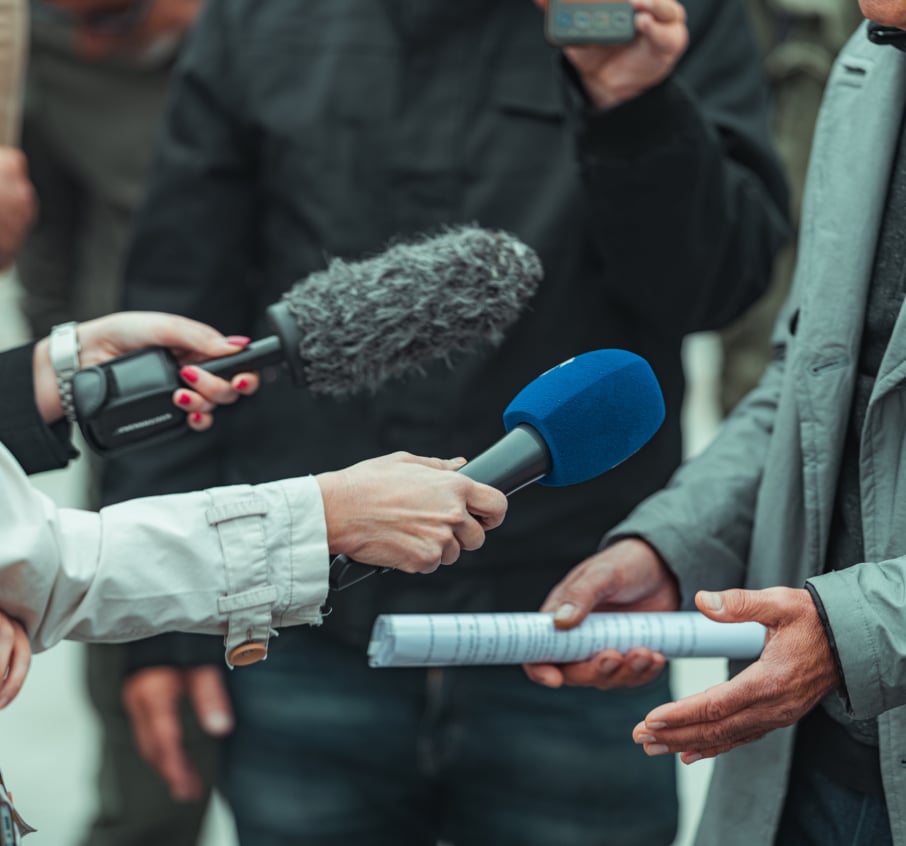 News reporters holding up microphones to a person they are trying to interview outside