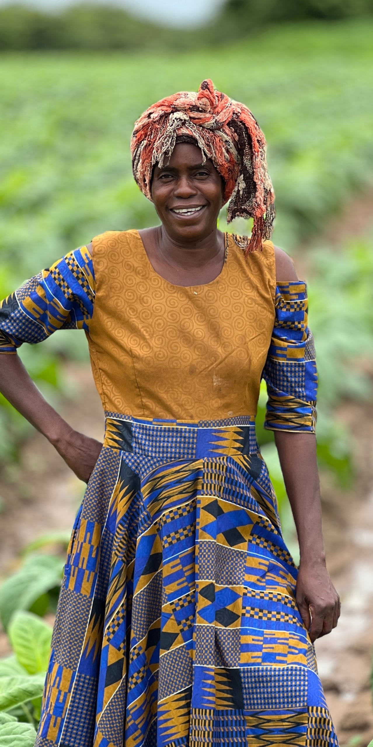 An African woman wearing traditional attire on a farm smiling at the camera