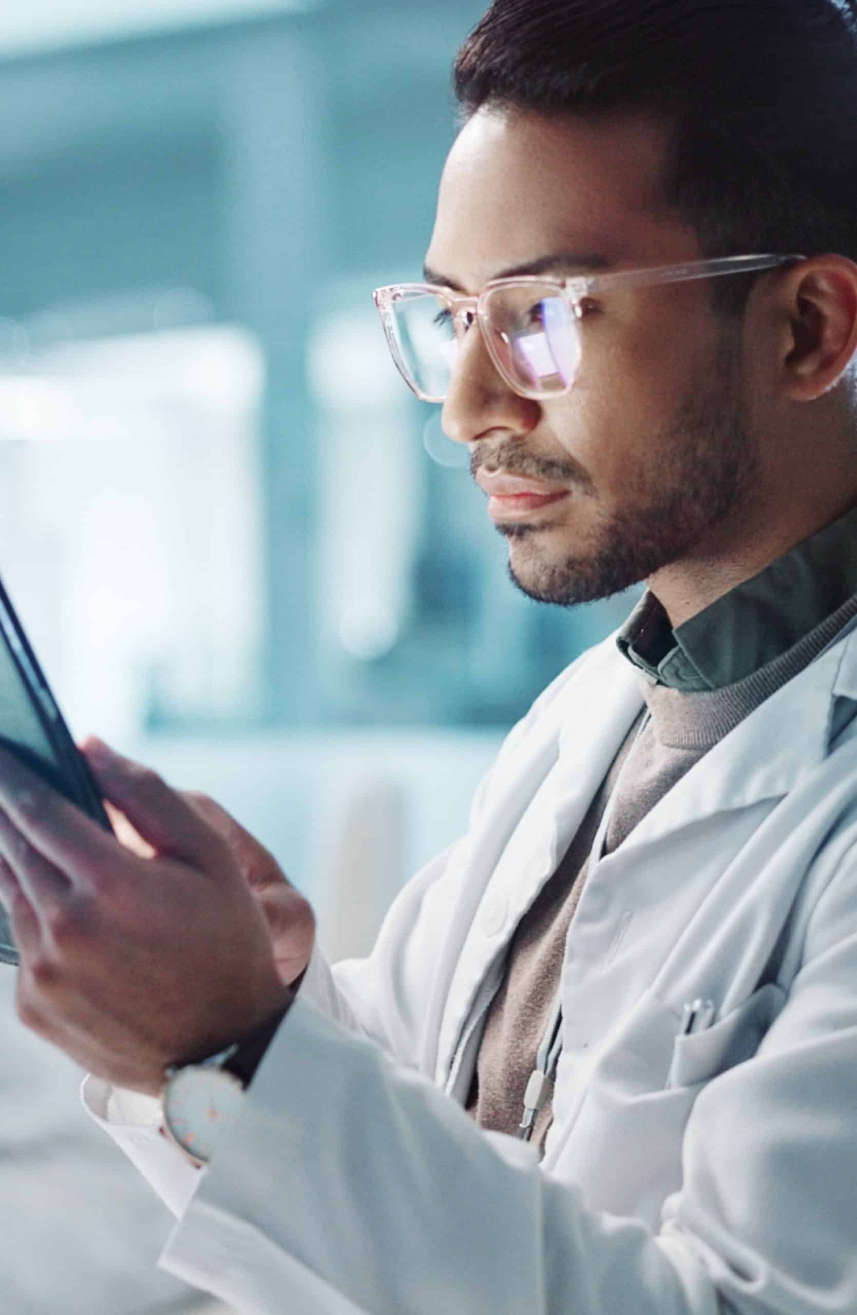 Man wearing glasses in a lab coat looking at a tablet device that he is holding