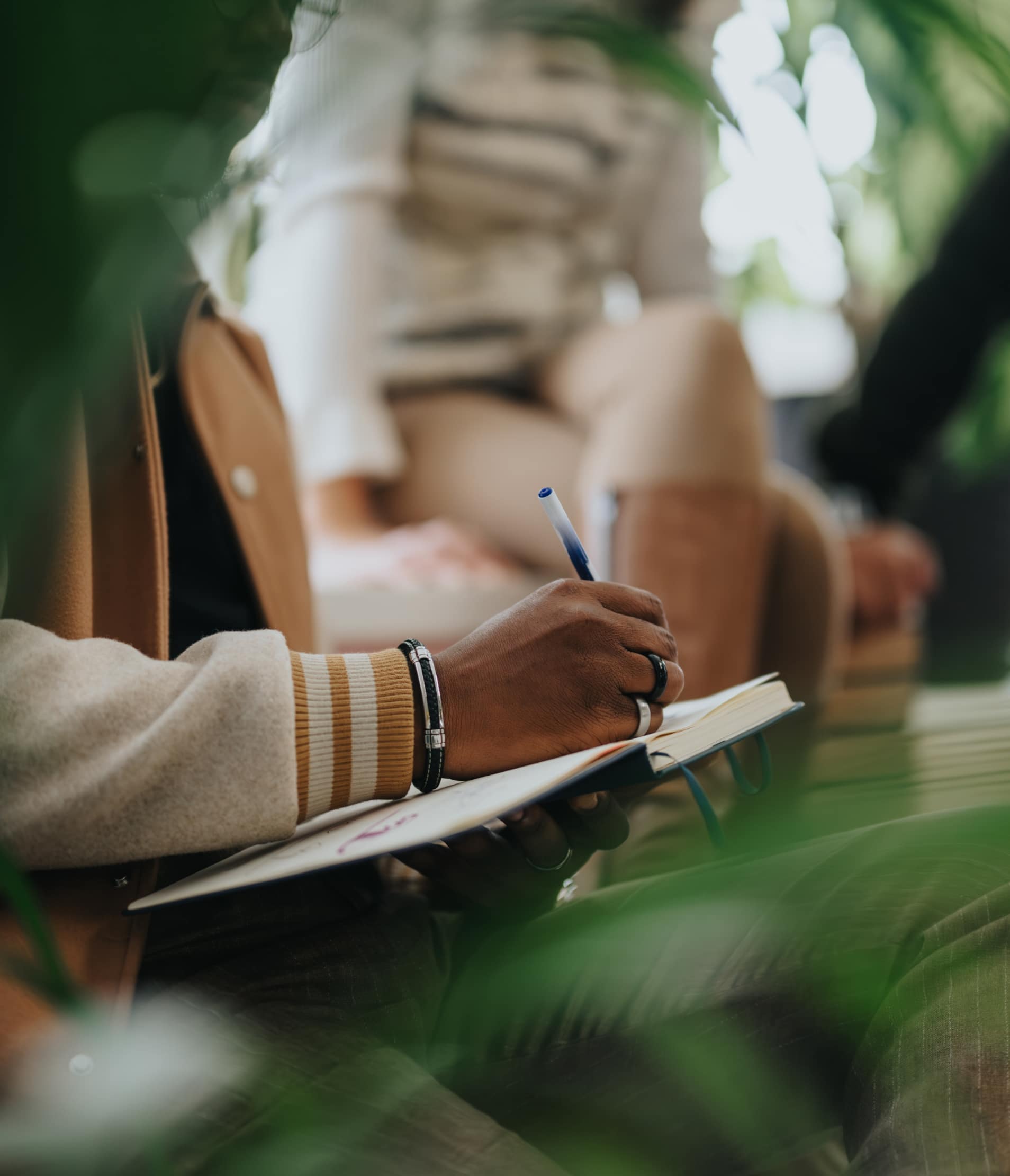 Woman sat down writing in a notebook with plants in the foreground