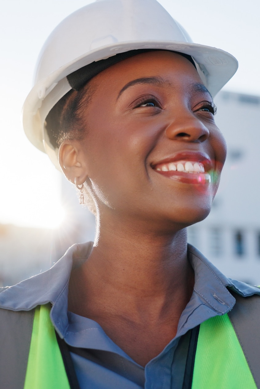 Woman wearing a hard hat and high visibility vest smiling and looking up at the sky