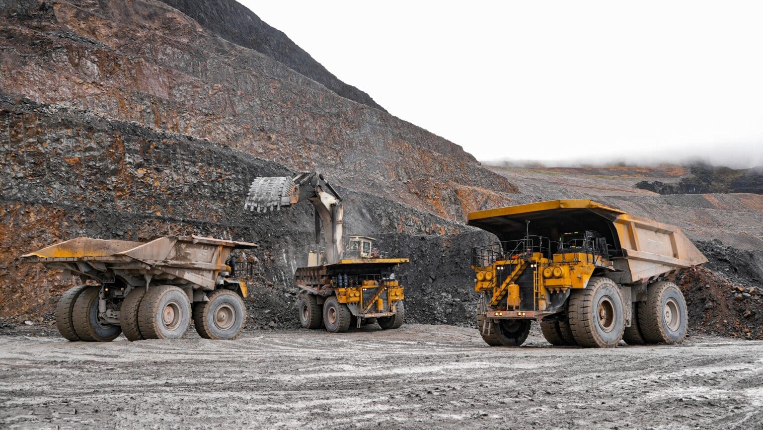 Large mining trucks and excavator in open-pit mine.